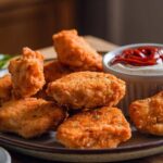 Plate of crispy homemade chicken nuggets with dipping sauce and fresh herbs
